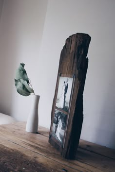 a vase with a plant in it next to a photo frame on a wooden table