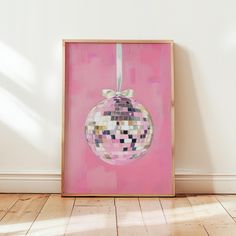 a pink painting with a disco ball hanging from it's side on a wooden floor