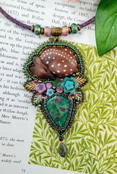 a necklace that is on top of a book with flowers and leaves around it, next to a green leaf