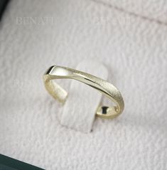 an open gold ring sitting on top of a white towel in a jewelry box,