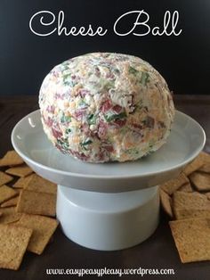 a cheese ball sitting on top of a white cake plate with crackers around it