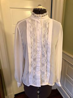 "This is an easy care yet professional blouse. This blouse is made of 100% polyester crepe and lace. There are no shoulder pads. It features a band collar with lace, front pearl button closure with vertical lace and a one inch tuck on either side. There are long sleeves with button cuffs, and a front pearl button closure. This garment is clean with no stains, snags, or odors. Measurements to guide you: Bust: 38\" Waist: 40\" Sleeve: 24\" Length from top of shoulder to hem: 26\" Decade: 70s Fabri Elegant Formal Blouse With Ruffled Collar, Elegant Formal Tops With Lace Sleeves, Classic Fitted Wedding Blouse, Feminine Blouse With Ruffled Collar For Formal Occasions, Elegant Tops With Ruffled Collar For Formal Events, Elegant Tops With Ruffled Collar For Formal Occasions, Fitted Formal Tops With Lace Cuffs, Fitted Formal Blouse With Lace Sleeves, Formal Fitted Tops With Lace Cuffs