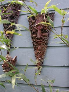 three masks are hanging on the side of a house with plants growing in front of them