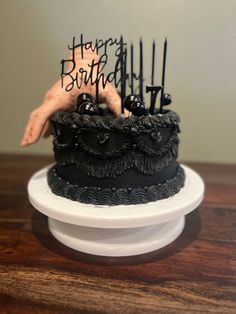 a black cake with candles on it sitting on top of a white plate next to a wooden table