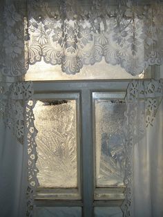 an open window with white lace curtains and frosted windowsills in front of it