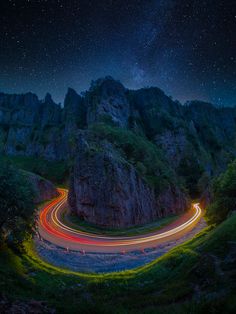 the night sky is filled with stars and light streaks as cars drive down a winding road