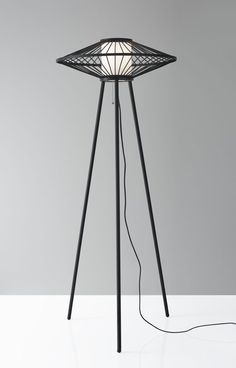 a floor lamp with a white light on top and black metal legs, in front of a gray wall