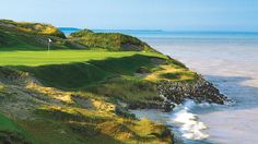 a golf course near the ocean with waves crashing on the sand and green grass in the foreground