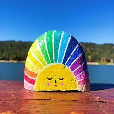 a colorful rock with a face painted on it sitting in front of a body of water