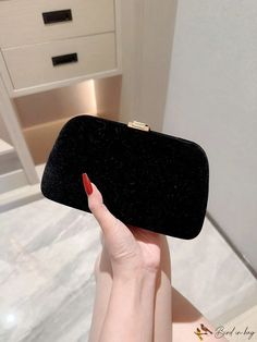 a woman's hand holding up a black velvet clutch bag in front of a mirror