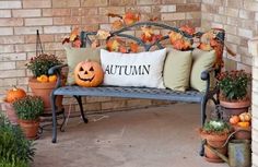 a bench that has some pumpkins on it and is sitting in front of a brick wall