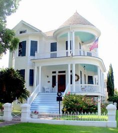 a large white house with blue shutters and american flags on the front porch is shown