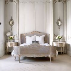 a bedroom with white furniture and mirrors on the walls, along with a bed that has two nightstands next to it