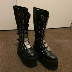 Brand New Demonia Platform Boots Size 7. Never Worn In Original Box. Platform Boots With Round Toe For Concert, Round Toe Platform Boots For Concert, Black Knee-high Platform Moto Boots, Black Edgy Moto Boots With Metal Pin Buckle, Edgy Black Moto Boots With Metal Pin Buckle, Gothic Boots With Buckle Closure And Round Toe, Platform Moto Boots For Concerts, Leather Moto Boots With Chunky Platform For Concert, Black Round Toe Boots For Concert