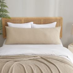 a bed with two pillows on top of it next to a lamp and a plant