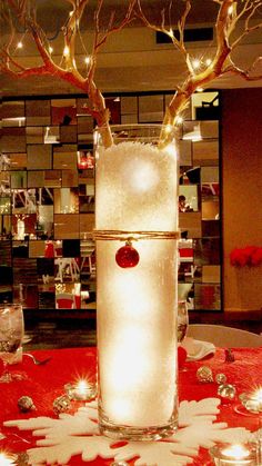 a tall glass vase filled with ice and lit candles on top of a red table cloth