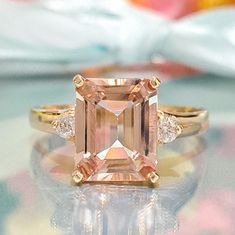 an orange and white diamond ring sitting on top of a glass table with flowers in the background