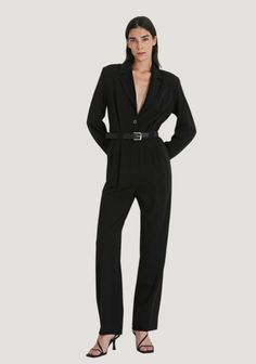 The Kala Jumpsuit from BYNIUMAAL is a stunning and versatile piece that can be worn for a variety of occasions. Its deep V-neckline and lapel detail add sophistication to its overall design. The long straight sleeves with three-button detail and shoulder pads provide a structured and elegant look that is universally timeless. The wide leg with pleats, high waist with belt detail and buckle create a flattering silhouette that is sure to turn heads. #WeddingGuestDress Formal Fall V-neck Jumpsuits And Rompers, Sleek Long Sleeve Semi-formal Pantsuit, Sleek Long Sleeve Pantsuit For Semi-formal Occasions, Sleek V-neck Jumpsuits And Rompers For Work, Sleek Long Sleeve Formal Pantsuit, V-neck Single Breasted Formal Suit, Formal V-neck Single Breasted Suits, Formal Single Breasted V-neck Suit, Single Breasted V-neck Suits For Formal Occasions