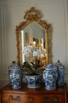 blue and white vases sit on a dresser with a mirror in the corner behind them