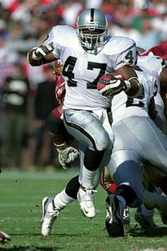 a football player running with the ball in his hand and other players on the field behind him