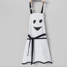 a white apron with black straps and a smiling face on the front, hanging from a hook