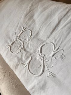 an embroidered pillow on top of a bed with white linens and decorative appliques