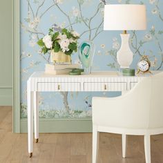 a white desk topped with a lamp next to a vase filled with flowers and a clock