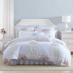 a white bed with blue and pink comforter in a room next to a window