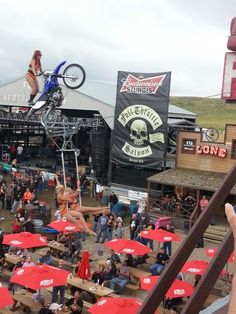 a person on a dirt bike jumping over tables with red umbrellas in the foreground