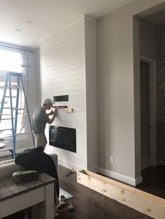 a man working on a fireplace in a living room with white walls and wood floors