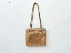 a gold purse hanging from a chain on a white wall, with the bottom part of it's flap closed