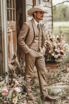 a man wearing a tan suit and hat standing in front of a building with flowers