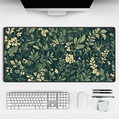 an overhead view of a computer keyboard, mouse and monitor on a white desk with green floral wallpaper