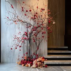 a tall vase with red flowers on top of a marble floor next to some stairs