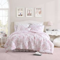 a bedroom with pink and white bedding, pictures on the wall and a window