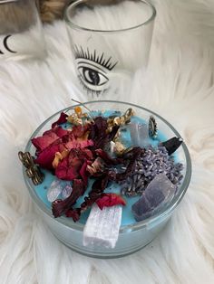 a bowl filled with flowers and rocks on top of a white fur covered floor next to two glasses