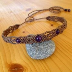 a brown bracelet with purple beads on top of a wooden table next to a rock