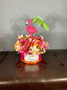 a pink flamingo sitting on top of a brown ottoman next to a flower pot