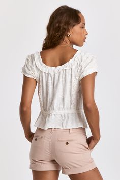 a woman is wearing shorts and a white top with ruffles on the back