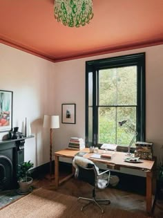 a room with a desk, chair and window in it that has a painting on the wall