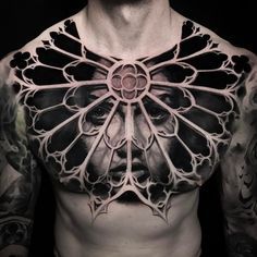 a man with tattoos on his chest is wearing an intricate piece of art that looks like a face