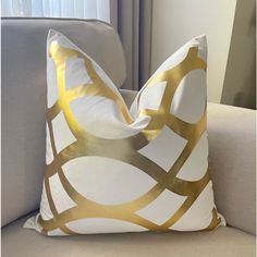 a white and gold pillow sitting on top of a gray couch next to a window