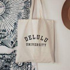 "DELULU UNIVERSITY TOTE BAG  Gift yourself or your delulu friends with this funny tote bag. This 100% cotton bag is 15\" x 16\" and perfect for everyday use.  Designed to tote your essentials, this tote bag features sturdy 20\" handles (made from the same canvas), making it easy to carry.  Designed with an appreciation for a minimal aesthetic, it will compliment any outfit.  Must have accessory for a day at the beach, to carry your school books or to run your daily errands. 🦋100% cotton canvas Tote Bag Print Design, Minimalist Tote Bag Design, Tote Bag Design Aesthetic, Custom Tote Bag Aesthetic, Delulu Aesthetic, Tote Bag Design Ideas Aesthetic, Toat Bag, Cool Tote Bag Design, Aesthetic Tote Bag Design