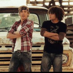 two young men standing in front of an old truck