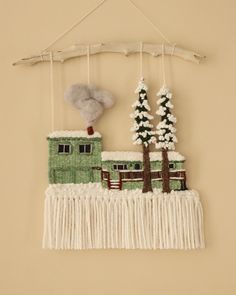 a wall hanging with a green house and trees in the snow on top of it