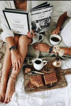 two people sitting on a bed reading books and having coffee with their feet propped up next to each other