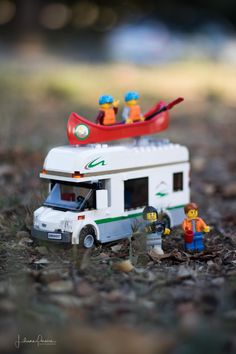 a toy camper with two people and a canoe on top is in the grass