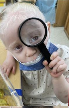 a young child holding a magnifying glass to look at something in front of her