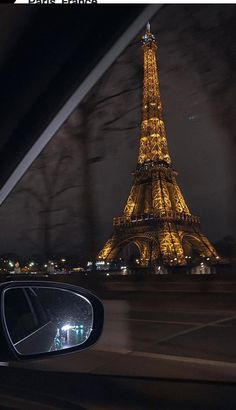 the eiffel tower is lit up at night from behind a car's side view mirror