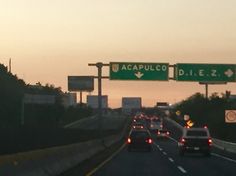 cars driving down the highway at dusk with street signs above them and traffic lights on either side